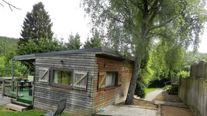 A small wooden cabin with a porch, a lawn chair, and a pathway leading to a wooden fence. - The charm of a wooden chalet with a magnificent view, not far from Spa (Stoumont)
