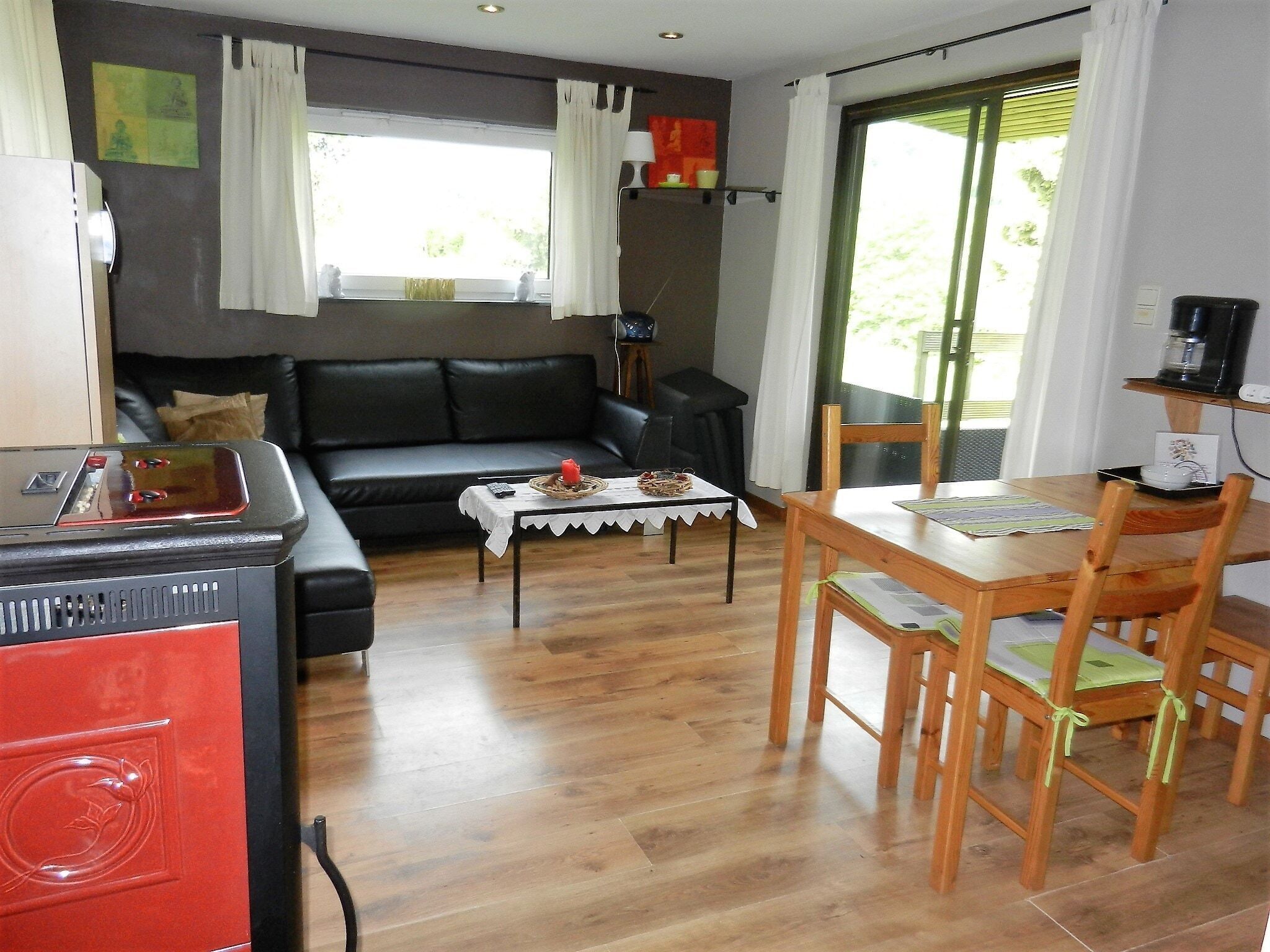 A living room with a black leather sofa, a small table with a white tablecloth, and a wooden dining table with chairs.
