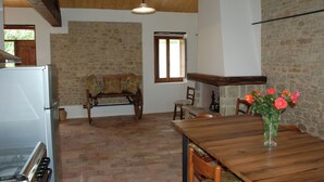 Una cocina rústica con pared de piedra, vigas de madera, una mesa de comedor con sillas, un banco de madera y un florero con flores.
