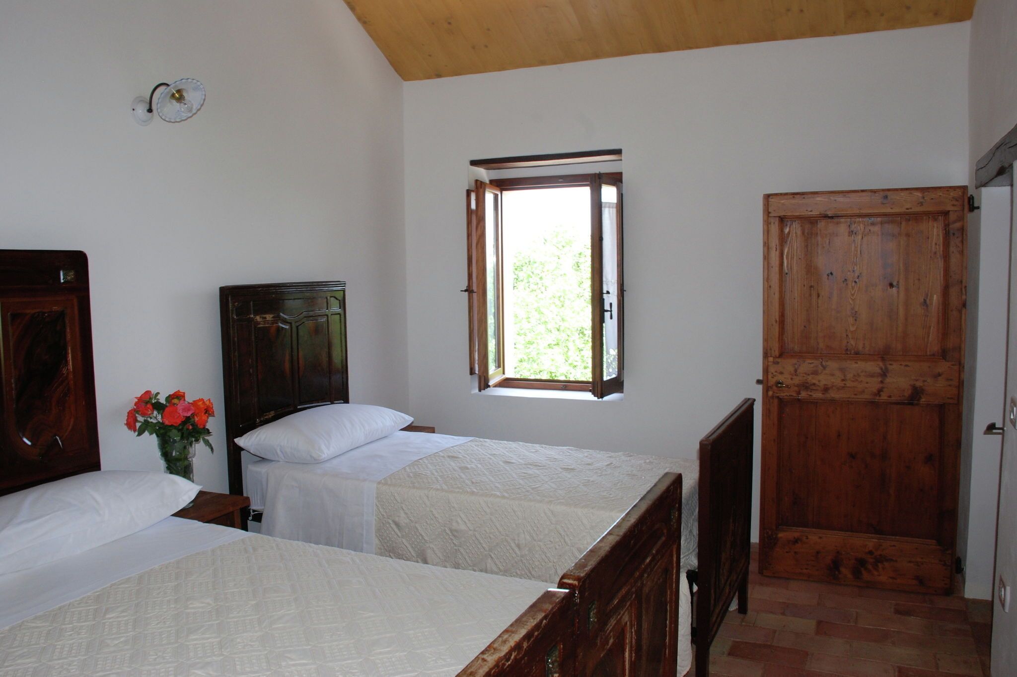 Ein Schlafzimmer mit zwei Betten, einem Holzschrank, einem Fenster mit Vorhängen und einer Wandleuchte.