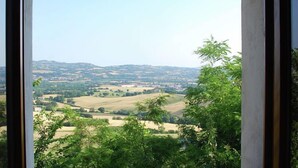 Vista a través de una ventana mostrando un paisaje rural, con campos y colinas lejanas.