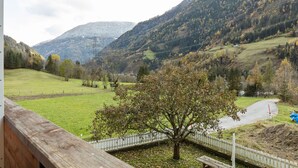 A view of a mountainous landscape with a wooden deck overlooking a grassy area and a small bridge. - Apartment in Matrei near Ski Slopes (Matrei in Osttirol)