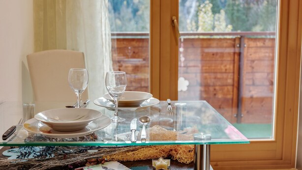 A dining table set with plates, glasses, and cutlery, with a view of a wooden fence and trees through a window. - Apartment in Matrei near Ski Slopes (Matrei in Osttirol)