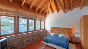 A bedroom with a wooden ceiling, stone wall, and a bed with a blue bedspread.
