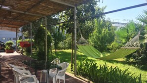 A covered patio with a table and chairs, a hammock, and lush greenery. - Belvilla by OYO Menotti (Trecase)