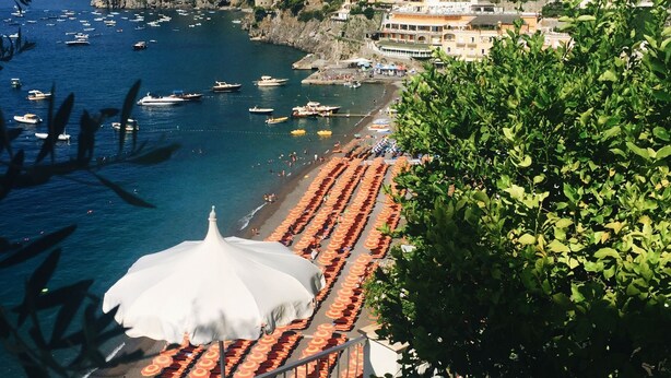 A coastal town with a beach lined with rows of umbrellas, boats in the water, and buildings on a hillside. - Belvilla by OYO Menotti (Trecase)