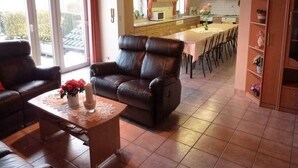 Un salon avec un canapé en cuir, une table basse ornée de fleurs et un coin repas comprenant une table et des chaises.