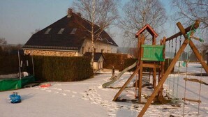 Un espace extérieur enneigé avec une structure de jeu en bois et une maison en arrière-plan.