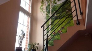 Un escalier orné d’une fresque représentant un arbre et des animaux, une fenêtre avec des plantes et un mur en briques.