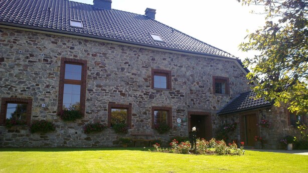 Un bâtiment en pierre avec un toit en tuiles, de nombreuses fenêtres et une pelouse bien entretenue agrémentée de fleurs.