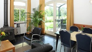 Une pièce avec une cheminée, une table à manger entourée de chaises, une grande plante en pot et une vue sur un jardin, visible à travers des portes vitrées.