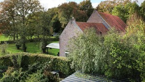 Un bâtiment en pierre avec un toit rouge, entouré d’une végétation luxuriante et d’arbres.