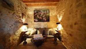 A cozy room with a wooden ceiling, stone walls, a sofa with cushions, two lamps, and a painting of flowers on the wall. - Cozy House in Lot with Pool and Terrace (Bon Encontre)