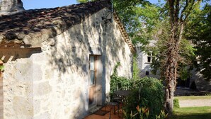 A rustic stone building with a tiled roof, a wooden door, and a small patio area with a table and chairs. - Cozy House in Lot with Pool and Terrace (Bon Encontre)
