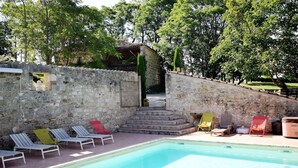 A stone wall with a pool and lounge chairs. - Cozy House in Lot with Pool and Terrace (Bon Encontre)