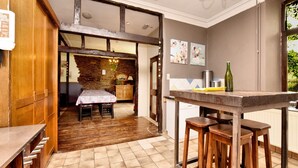 Una cocina con una mesa de madera y taburetes, una pared de piedra y un comedor con mesa y sillas.