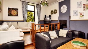 Un salón acogedor con un sofá, una mesa de centro y una chimenea. Hay un televisor y un reloj en la pared.