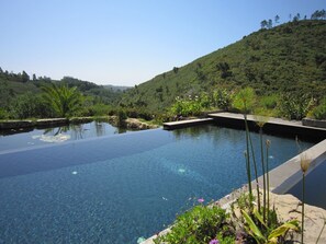 Ein klarer, blauer Infinity-Pool, umgeben von üppiger Vegetation und einer Hügelsicht.