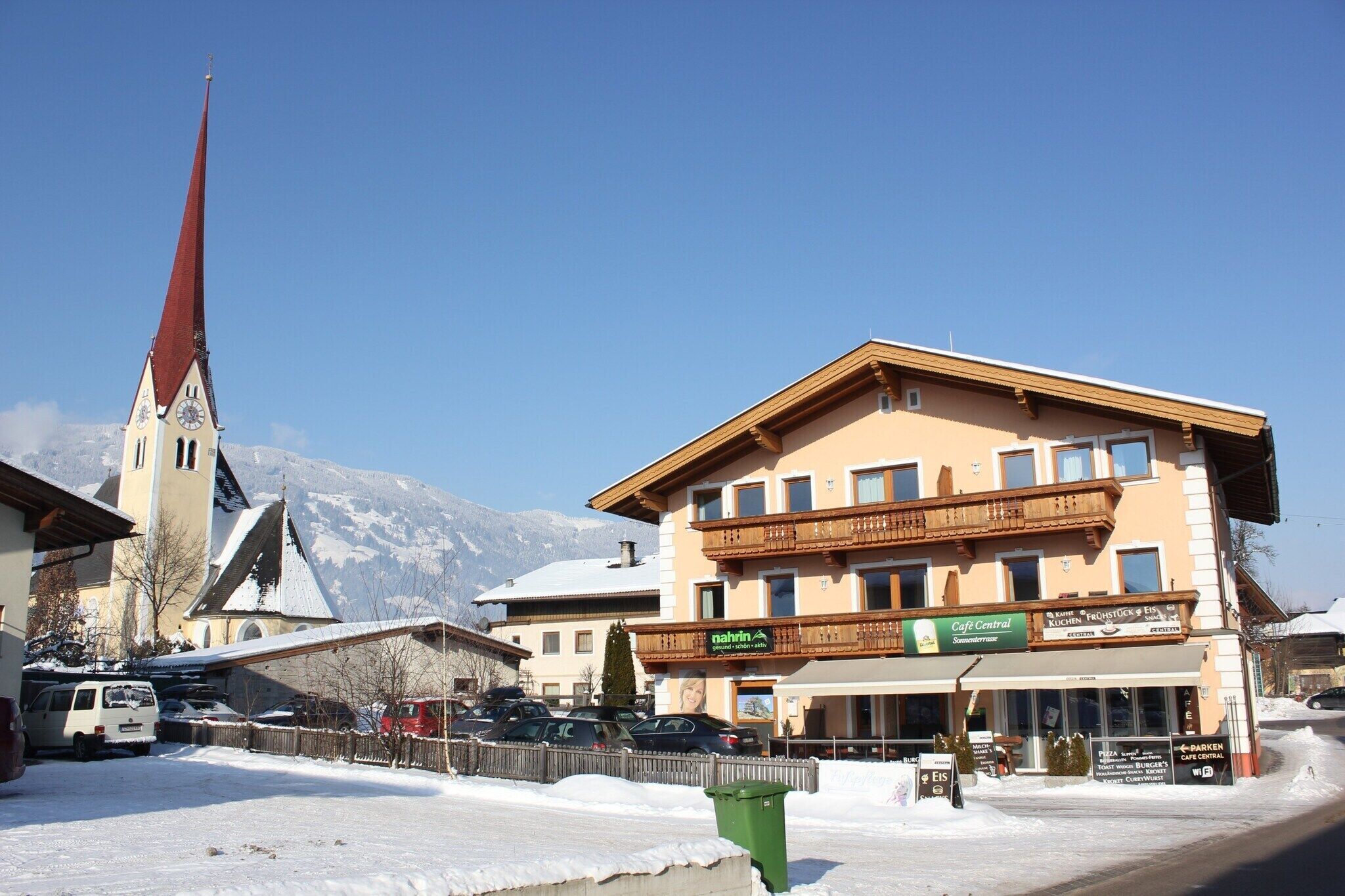 A hotel with a balcony, a clock tower, and a mountain backdrop.