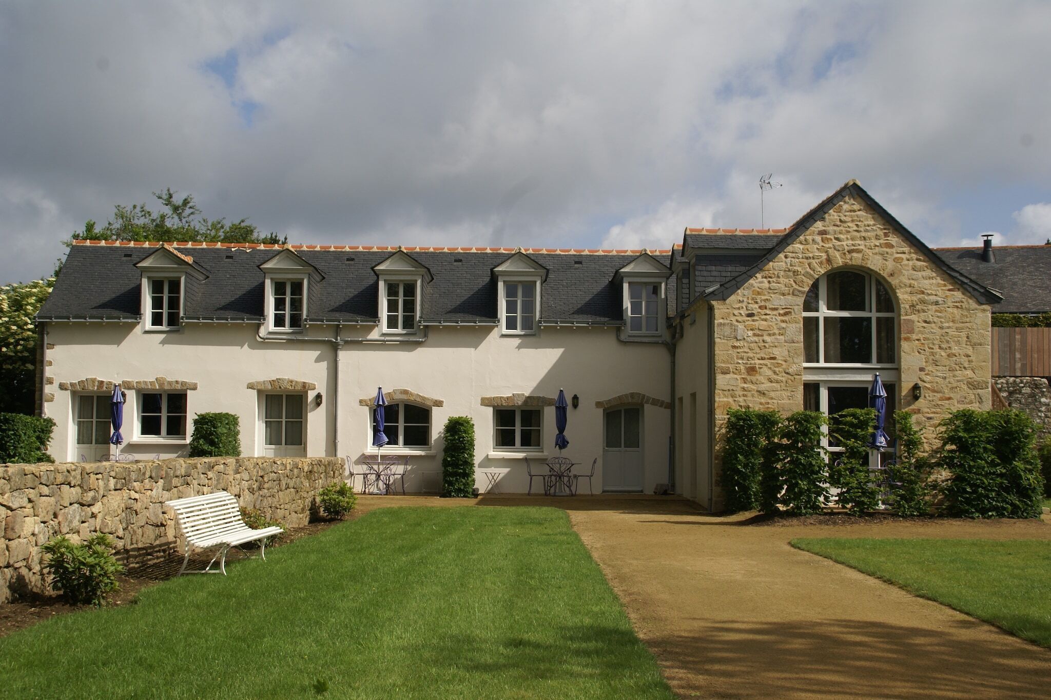 Une maison en pierre à deux étages, dotée d’une façade en pierre, de nombreuses fenêtres et d’une pelouse bien entretenue.
