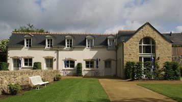 Une maison en pierre à deux étages, dotée d’une façade en pierre, de nombreuses fenêtres et d’une pelouse bien entretenue.