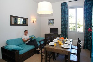 A living room with a sofa, a dining table set for breakfast, a television, and a window with curtains. - Apartment in Erdeven near Kerhillio Beach (Erdeven)