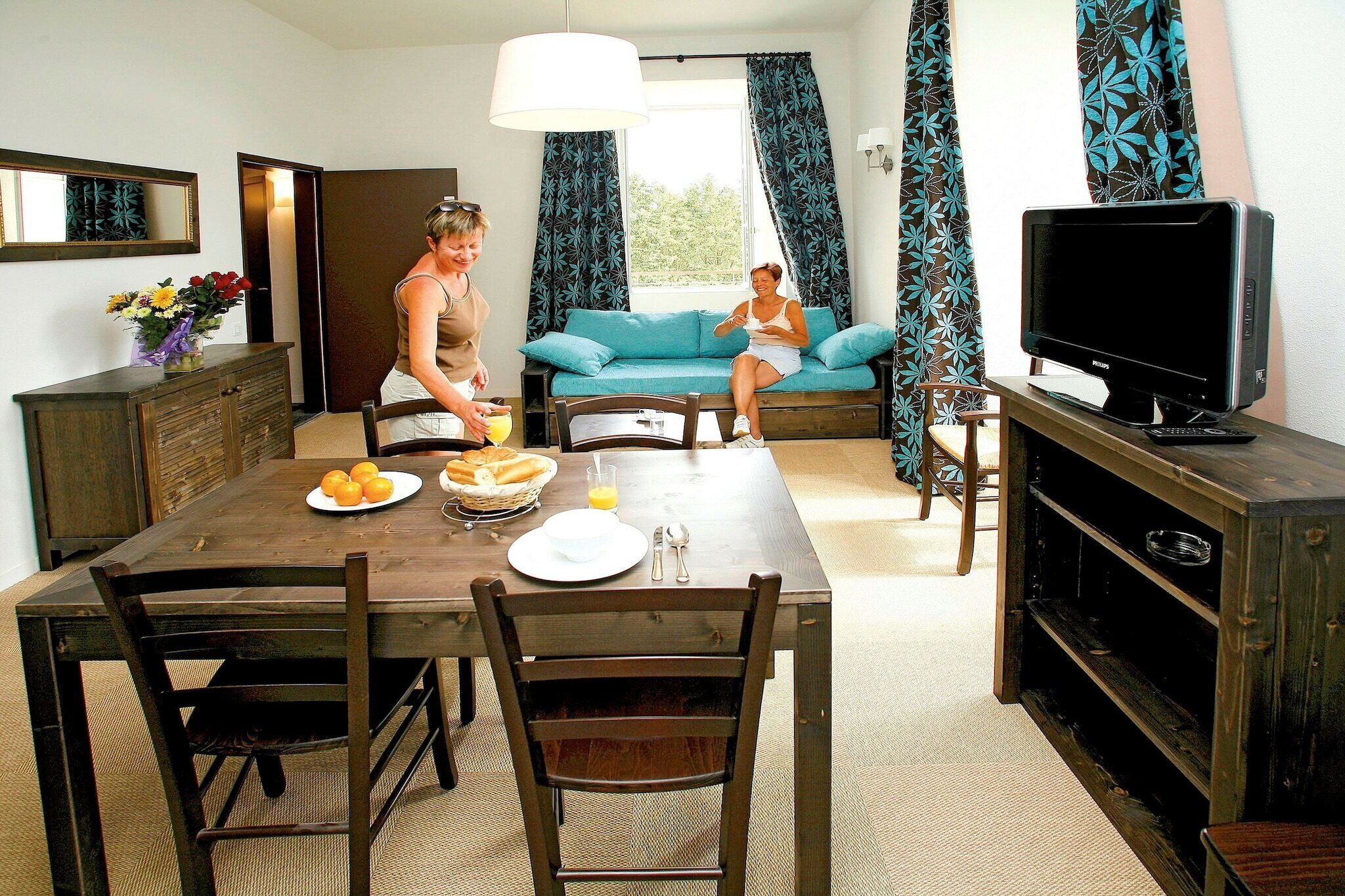 Un coin repas avec une table dressée pour deux personnes, un téléviseur et un canapé en arrière-plan.