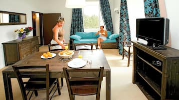 Un coin repas avec une table dressée pour deux personnes, un téléviseur et un canapé en arrière-plan.