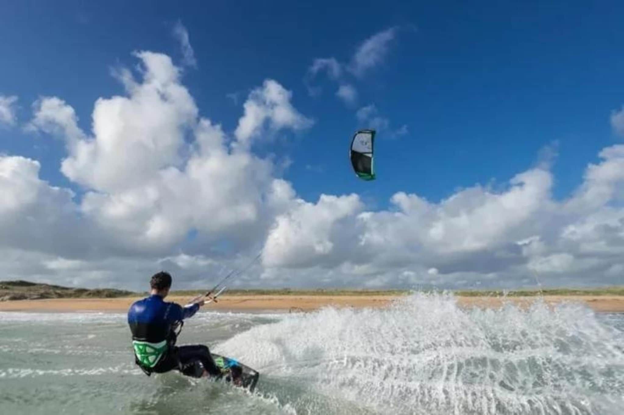 Una persona practicando windsurf en una masa de agua, con cielo despejado y nubes al fondo.