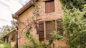 A rustic stone building with wooden shutters, surrounded by lush greenery and flowering vines. - Holiday Home in Dordogne near Lascaux Cave (Les Eyzies-De-Tayac-Sireuil)