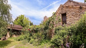A rustic stone building with a thatched roof, surrounded by lush greenery and flowering plants. - Holiday Home in Dordogne near Lascaux Cave (Les Eyzies-De-Tayac-Sireuil)