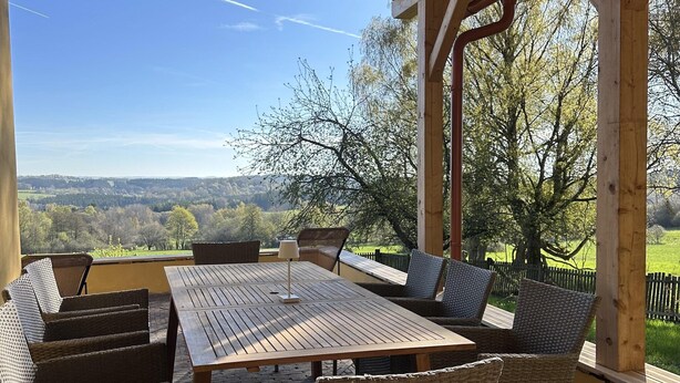 Een overdekt buitengebied met een tafel en stoelen, met uitzicht op een prachtig landschap.