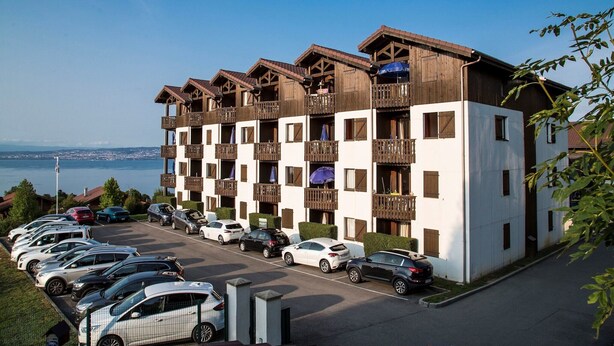 A multi-story hotel with balconies, a parking lot, and a view of the sea. - Apartment in Evian with Lake Geneva View (Bernex)
