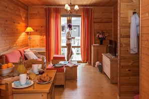 A cozy cabin interior with a sofa, dining table, and a person standing by a window.