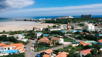 A coastal town with a mix of residential and commercial buildings, a beach in the background, and a clear sky.