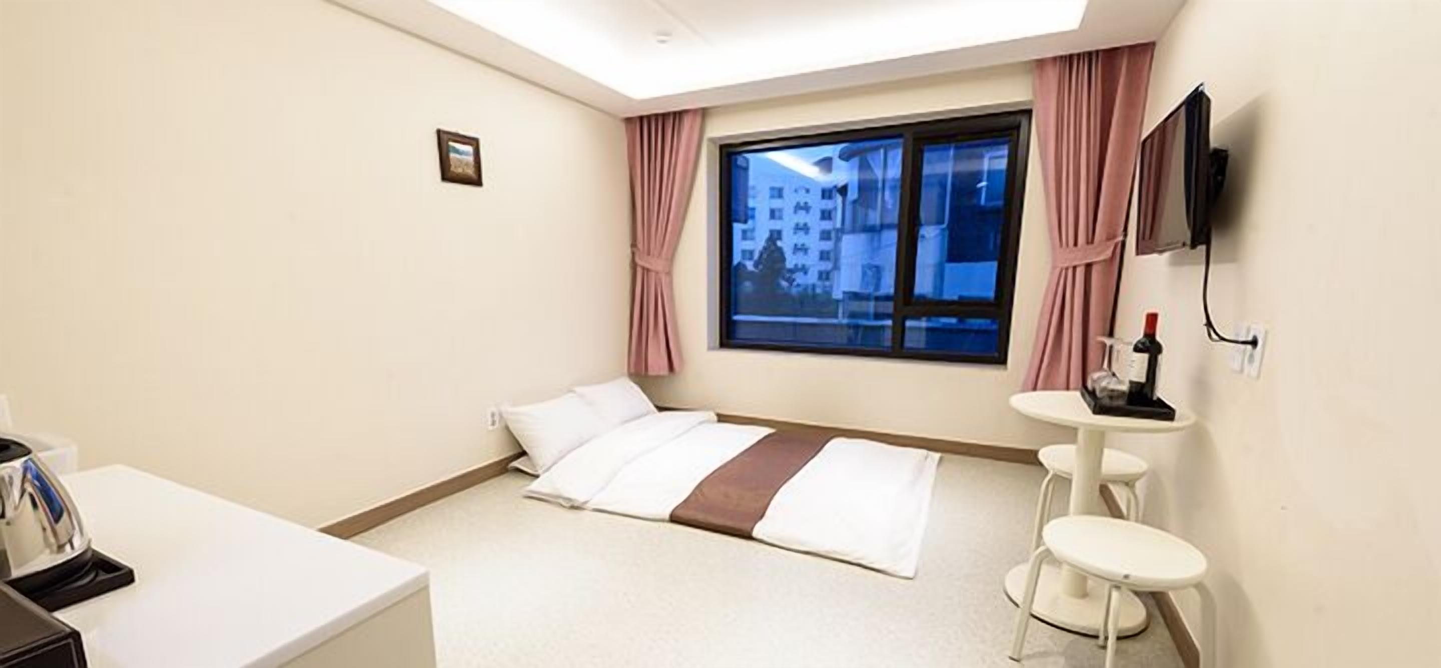 A hotel room with a bed, a desk, a chair, a TV, and a window with curtains.