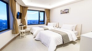 Habitació d'hotel amb dos llits, televisió, taula petita i finestra amb vista a la ciutat.