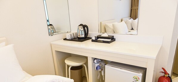 A hotel room with a white vanity, a mirror, a sink, a small stool, a hairdryer, a kettle, and a fire extinguisher. - Rezion Tourist Hotel (Seogwipo)