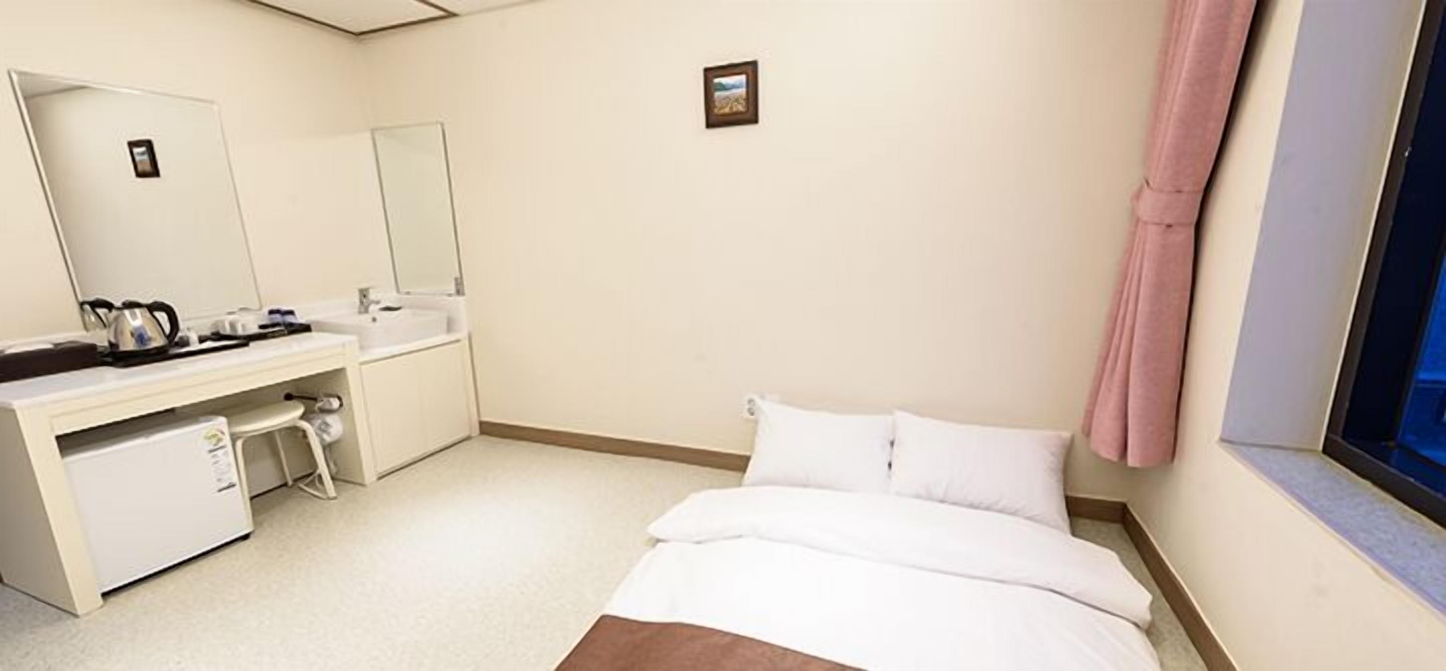 Une chambre d’hôtel avec un lit, un bureau doté d’un miroir, un lavabo et une fenêtre avec des rideaux.