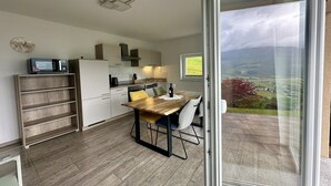 Une cuisine moderne avec un coin repas, un four à micro-ondes et une vue sur la campagne, visible à travers une porte vitrée.