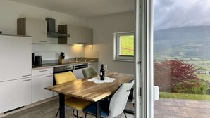 Une cuisine moderne avec une table à manger, des chaises et une vue sur la campagne, visible à travers une grande fenêtre.