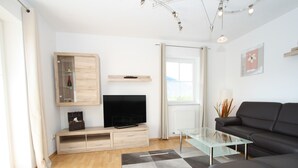 Un soggiorno moderno con una TV a schermo piatto, mobili contenitori in legno, un tavolino da caffè in vetro, un divano nero e un tappeto a scacchi.