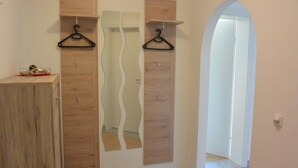 Un corridoio con rivestimenti in legno, uno specchio e due appendini neri su una mensola di legno.