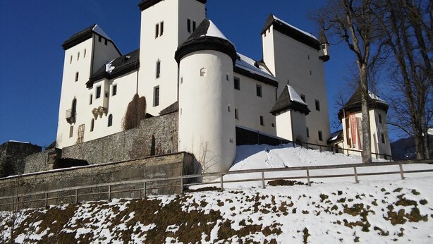 Un grande e storico castello con numerose torri e una torre centrale imponente, circondato da terreno innevato.