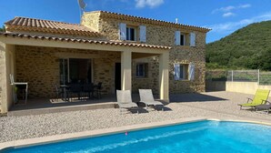 A two-story stone building with a swimming pool, outdoor seating, and a view of a green hill. - Beautiful villa with private pool in Gard (St.Laurent de Carnols)