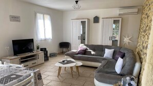 A living room with a sofa, a TV, a dining table, and a small table with decorative items. - Beautiful villa with private pool in Gard (St.Laurent de Carnols)