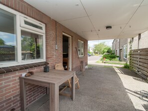 Enjoy dining or relaxing on the patio, surrounded by lush greenery and a charming brick building.
