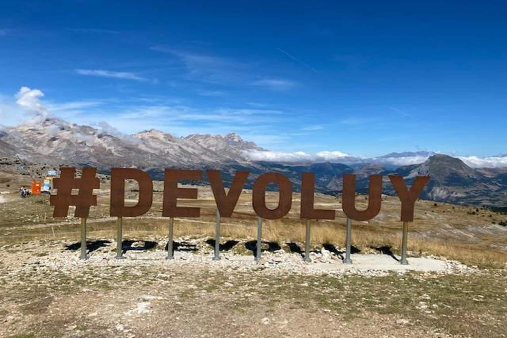 Ein Schild mit dem Text '#DEVOLUY' vor einer gebirgigen Landschaft.