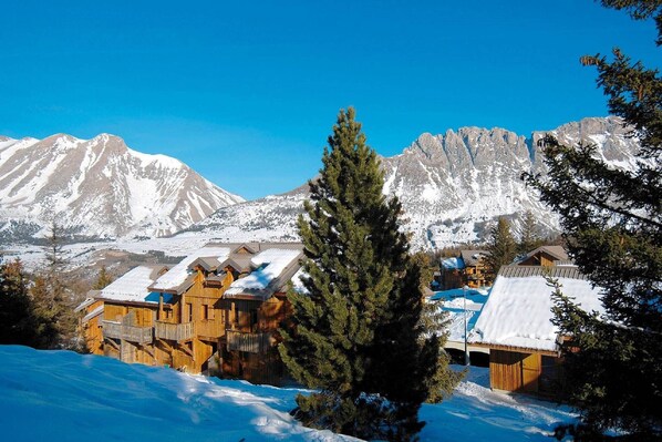 A snow-covered mountain landscape with wooden cabins and a clear blue sky. - Spacious Alpine Chalet (Le Devoluy)