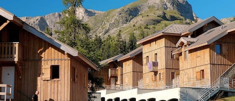 A row of wooden mountain cabins with a mountain backdrop.